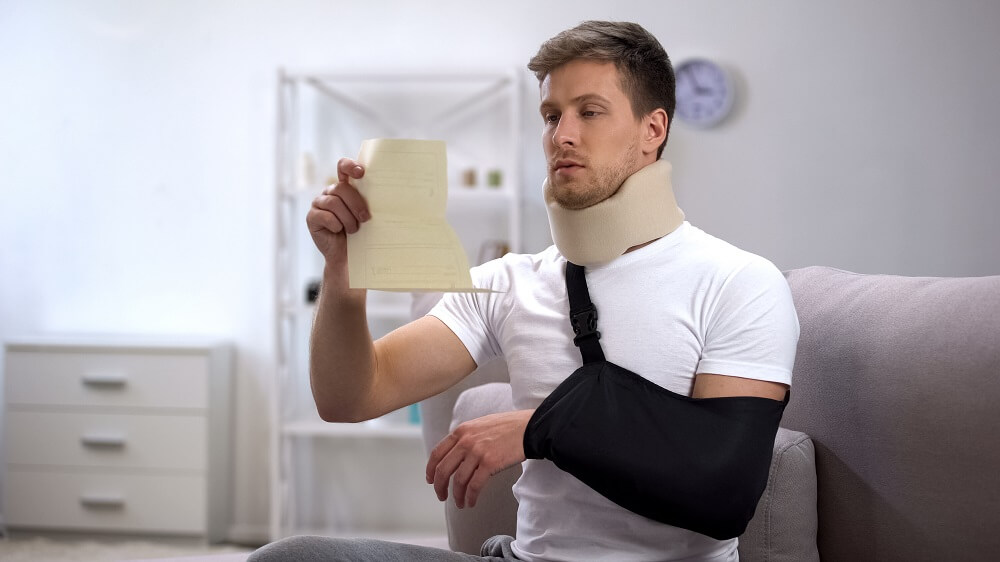 Injured man with cervical collar and arm sling reading medical bills.