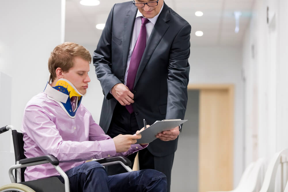 Injured employee on wheelchair submitting workers compensation claim form to lawyer.